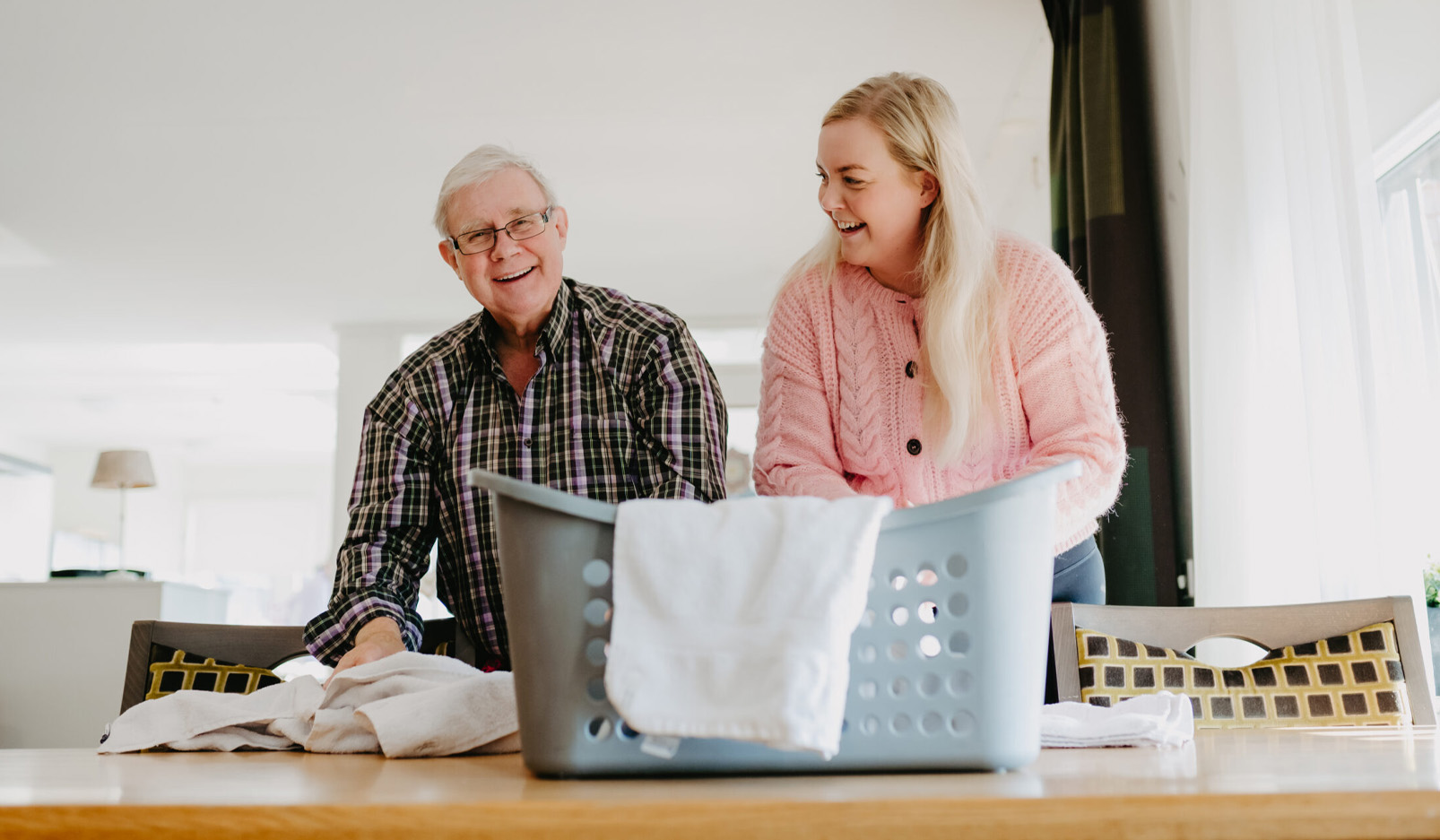 Oudere man en vrouw doen samen de was en lachen in een huiselijke omgeving